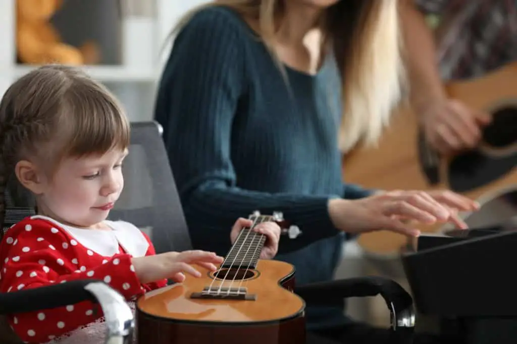 child learning ukulele next to mother playing piano